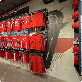 Wanddruck mit FC Bayern Vereinsfarben im Fanshop – rote Trikots vor gestalteter Betonwand