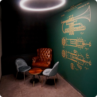 Wanddruck Thomann Showroom – goldene Trompeten-Blaupause auf dunkelgrüner Putzwand mit Ledersesseln